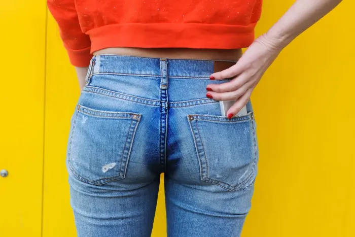 The back of a pair of blue jeans with a dark sweat stain running down the seat.